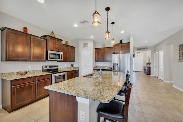 kitchen with a kitchen breakfast bar, pendant lighting, stainless steel appliances, sink, and an island with sink