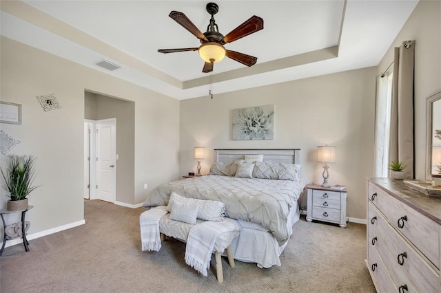 carpeted bedroom with ceiling fan and a tray ceiling