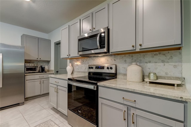 kitchen with stainless steel appliances, backsplash, light tile patterned flooring, light stone counters, and gray cabinetry