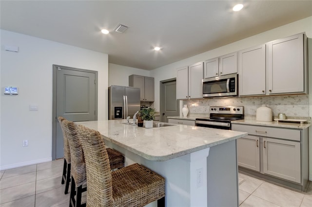 kitchen featuring appliances with stainless steel finishes, sink, gray cabinetry, light tile patterned floors, and a kitchen island with sink