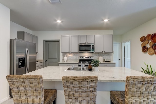 kitchen featuring gray cabinets, an island with sink, a breakfast bar, and appliances with stainless steel finishes