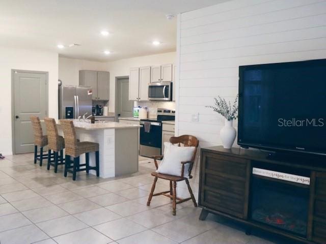 kitchen featuring appliances with stainless steel finishes, light tile patterned floors, gray cabinets, a kitchen island with sink, and a breakfast bar