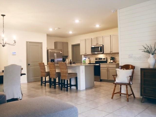 kitchen with decorative light fixtures, stainless steel appliances, an island with sink, a kitchen breakfast bar, and light tile patterned floors