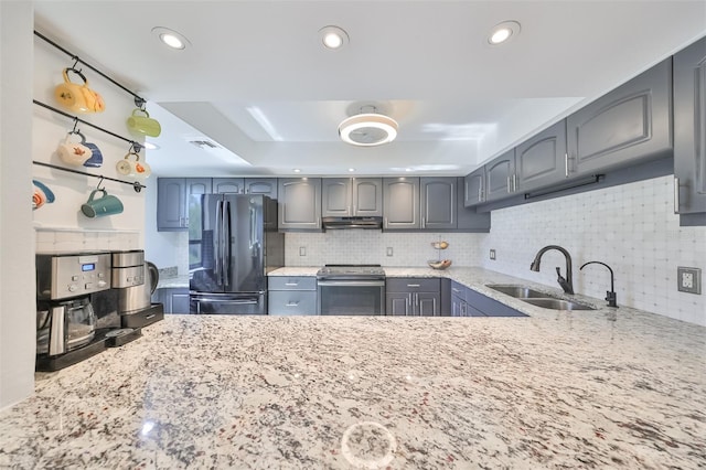 kitchen with gray cabinetry, stainless steel appliances, light stone counters, sink, and tasteful backsplash