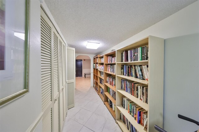 corridor with a textured ceiling and light tile floors