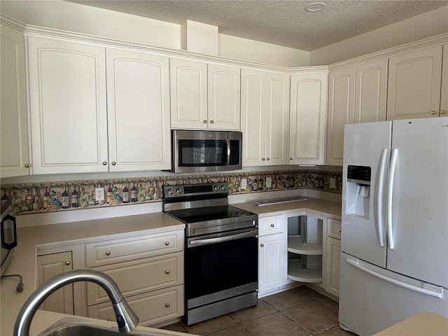 kitchen featuring stainless steel appliances, white cabinetry, dark tile floors, and a textured ceiling