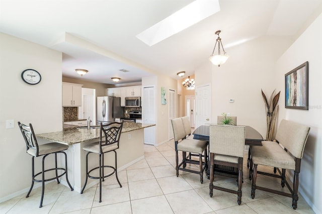 dining room featuring sink, lofted ceiling with skylight, and light tile floors