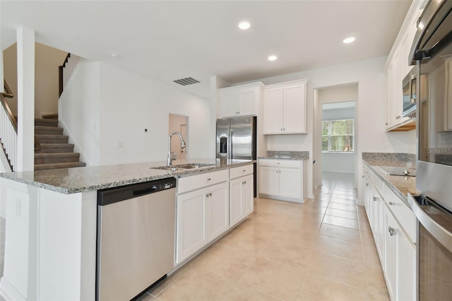 kitchen with sink, appliances with stainless steel finishes, white cabinetry, light stone countertops, and a center island with sink