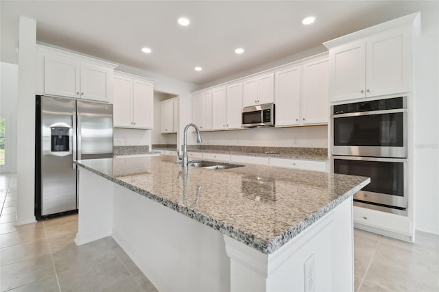 kitchen featuring an island with sink, sink, white cabinets, light stone counters, and stainless steel appliances