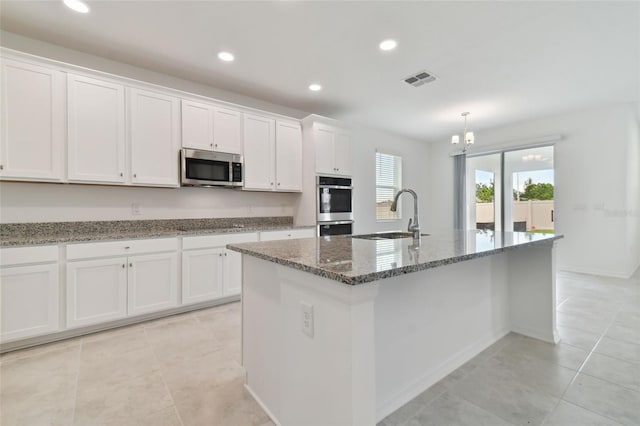 kitchen with sink, dark stone counters, an island with sink, stainless steel appliances, and white cabinets