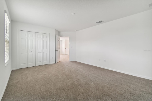unfurnished bedroom featuring multiple windows, carpet flooring, and a closet