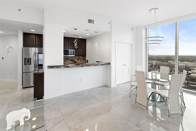 kitchen with dark stone countertops, dark brown cabinets, backsplash, hanging light fixtures, and appliances with stainless steel finishes