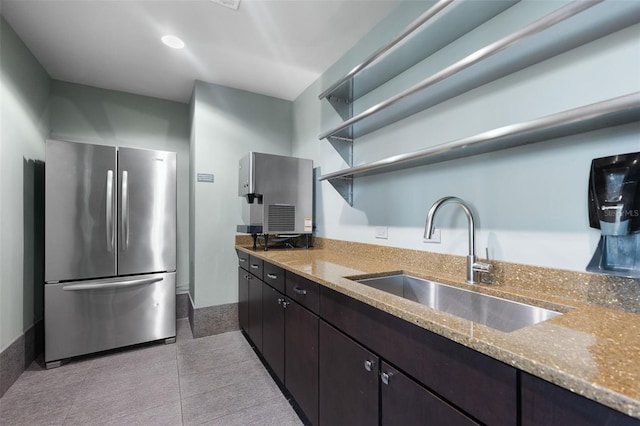 kitchen featuring light tile patterned floors, light stone countertops, sink, stainless steel fridge, and dark brown cabinetry