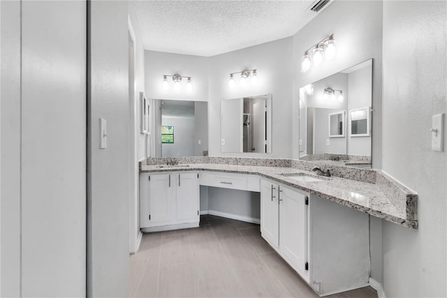 bathroom featuring a textured ceiling, dual bowl vanity, and tile flooring