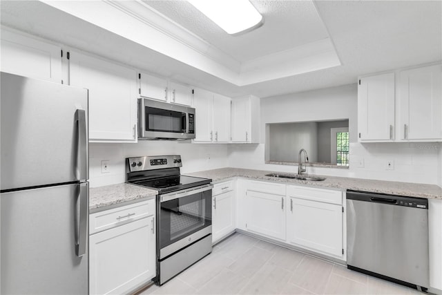 kitchen with appliances with stainless steel finishes, white cabinetry, sink, and a tray ceiling