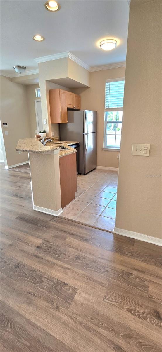 kitchen featuring light wood-type flooring, sink, kitchen peninsula, stainless steel refrigerator, and crown molding