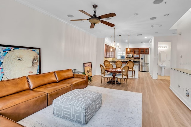 living room featuring light hardwood / wood-style floors, ceiling fan with notable chandelier, and crown molding