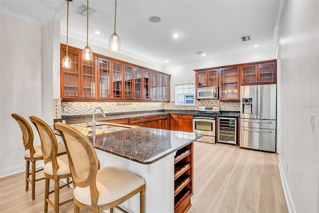 kitchen featuring decorative light fixtures, stainless steel appliances, light hardwood / wood-style floors, beverage cooler, and sink