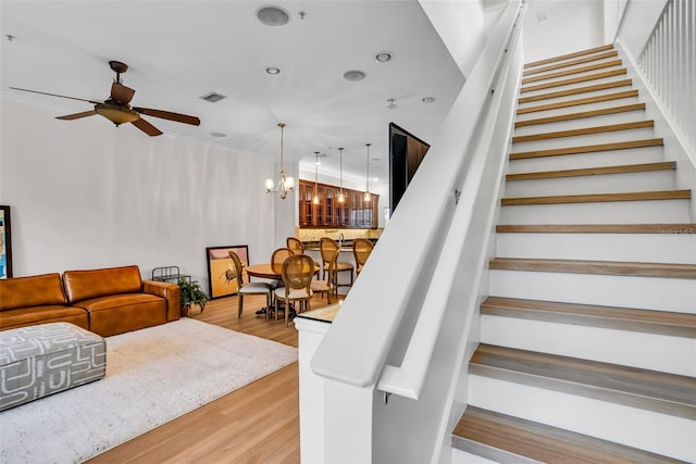 stairs featuring ceiling fan with notable chandelier and light wood-type flooring