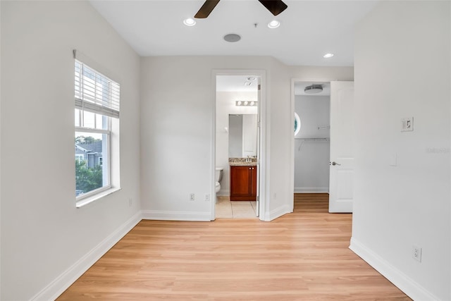 unfurnished bedroom with connected bathroom, ceiling fan, a spacious closet, and light wood-type flooring