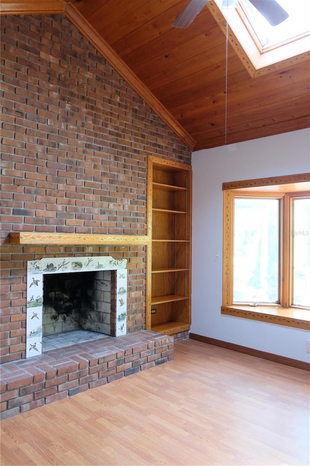 unfurnished living room featuring a fireplace, brick wall, wood-type flooring, lofted ceiling with skylight, and ceiling fan