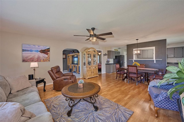 living room with ceiling fan with notable chandelier and light wood-type flooring