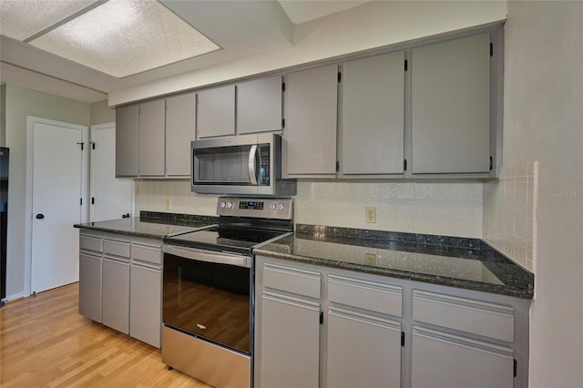 kitchen featuring light hardwood / wood-style flooring, gray cabinets, stainless steel appliances, tasteful backsplash, and dark stone counters