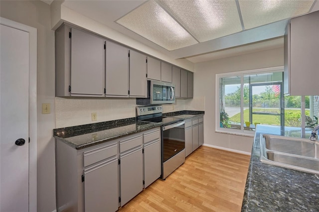 kitchen with appliances with stainless steel finishes, sink, light wood-type flooring, gray cabinetry, and dark stone countertops