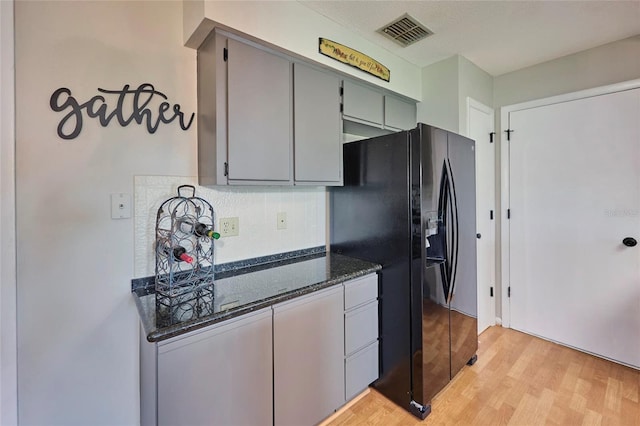 kitchen with backsplash, light wood-type flooring, gray cabinets, dark stone counters, and black refrigerator with ice dispenser