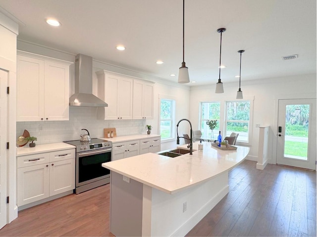 kitchen with stainless steel electric range oven, hardwood / wood-style floors, an island with sink, wall chimney exhaust hood, and sink