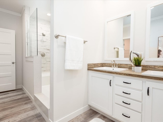 bathroom featuring a shower, dual bowl vanity, hardwood / wood-style flooring, and ornamental molding