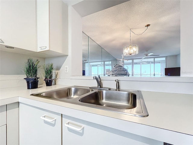 kitchen featuring ceiling fan with notable chandelier, a textured ceiling, white cabinets, and sink