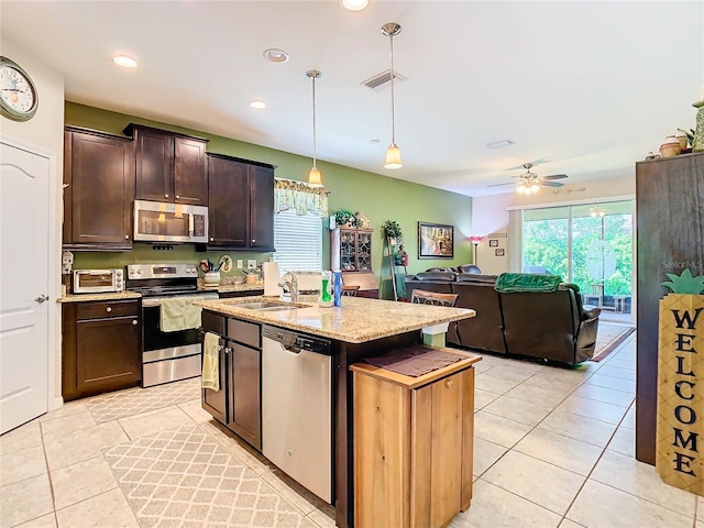 kitchen with ceiling fan, sink, decorative light fixtures, stainless steel appliances, and a center island with sink