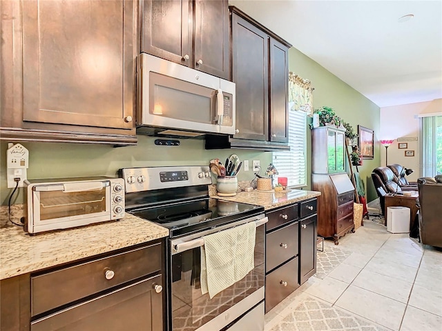 kitchen with dark brown cabinets, stainless steel appliances, light tile floors, and light stone counters