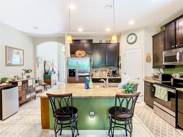 kitchen featuring a kitchen breakfast bar, light stone countertops, appliances with stainless steel finishes, light tile floors, and a center island with sink