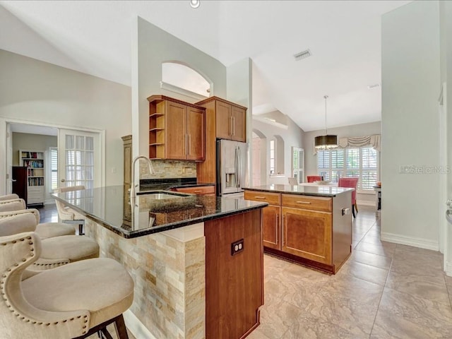 kitchen with light tile floors, decorative light fixtures, lofted ceiling, an island with sink, and stainless steel refrigerator with ice dispenser