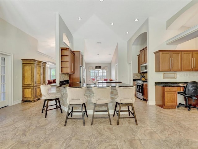 kitchen with high vaulted ceiling, appliances with stainless steel finishes, decorative light fixtures, and a breakfast bar