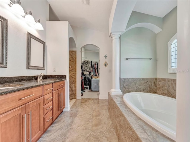 bathroom with tile floors, vaulted ceiling, double sink vanity, ornate columns, and tiled bath