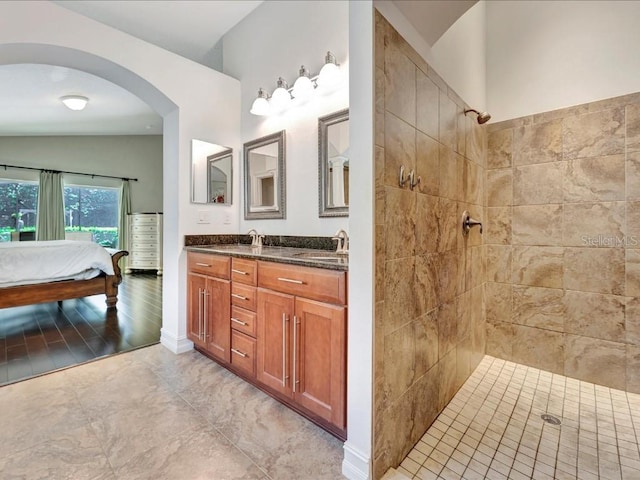 bathroom with oversized vanity, a tile shower, lofted ceiling, double sink, and tile floors