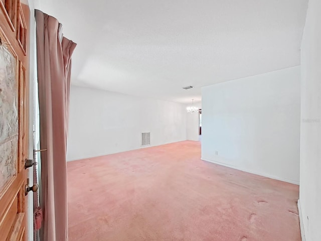 unfurnished room featuring a textured ceiling, light carpet, and a chandelier