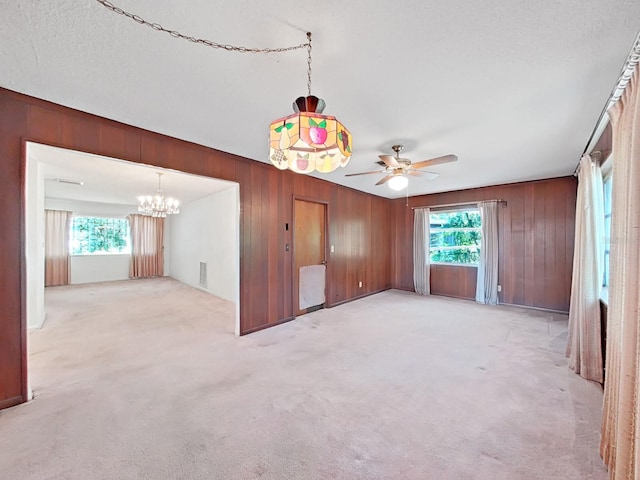 empty room featuring light colored carpet, a textured ceiling, wood walls, and ceiling fan with notable chandelier