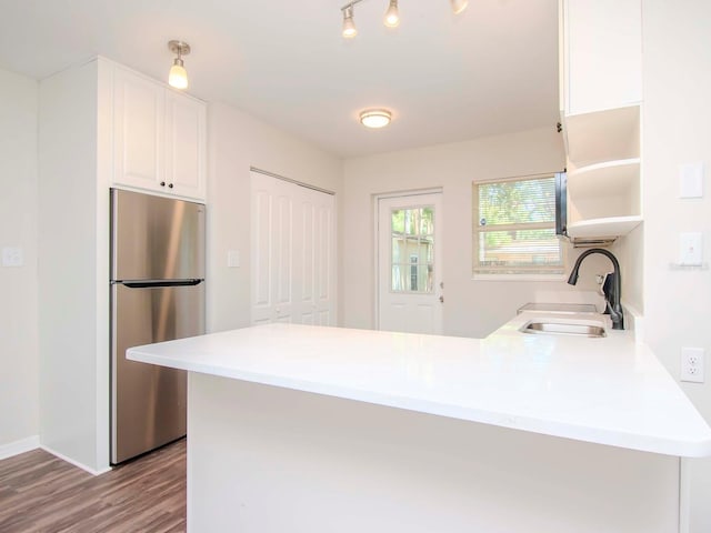 kitchen with white cabinets, stainless steel refrigerator, kitchen peninsula, sink, and hardwood / wood-style flooring