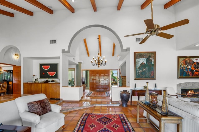 tiled living room with ceiling fan with notable chandelier, beamed ceiling, a towering ceiling, and a fireplace