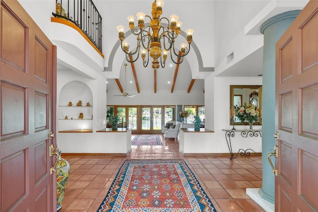 tiled entrance foyer featuring french doors, a towering ceiling, beamed ceiling, and ceiling fan with notable chandelier