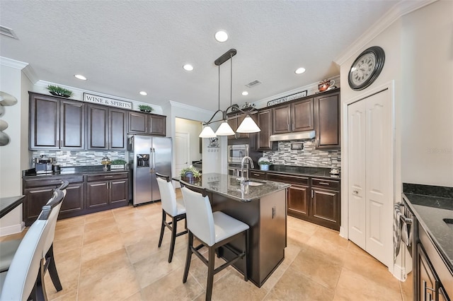 kitchen featuring backsplash, appliances with stainless steel finishes, a kitchen island with sink, and light tile floors