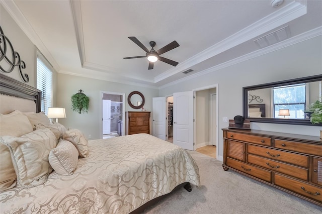 bedroom with ensuite bathroom, light carpet, ceiling fan, and a tray ceiling