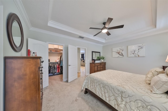 bedroom with light colored carpet, a closet, a walk in closet, and a tray ceiling