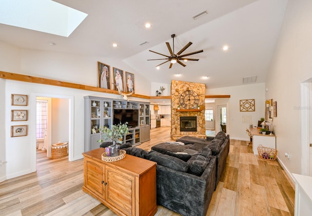 living room with high vaulted ceiling, a fireplace, light wood-type flooring, a skylight, and ceiling fan