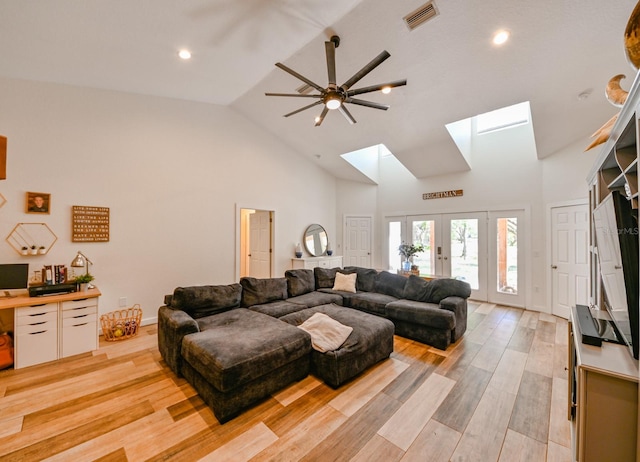 living room featuring high vaulted ceiling, french doors, light hardwood / wood-style flooring, a skylight, and ceiling fan