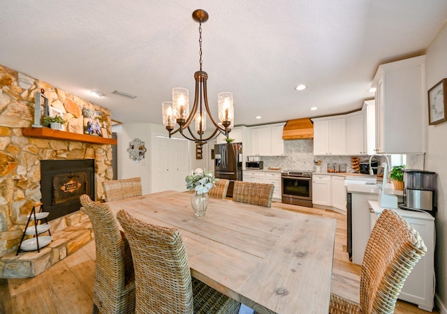 dining space featuring sink, light hardwood / wood-style floors, a fireplace, and an inviting chandelier